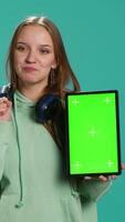 Vertical Portrait of woman presenting tablet with chroma key display, isolated over studio background. Young girl creating promotion with blank copy space mockup digital device, camera A video