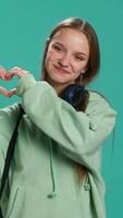 vertikal porträtt av vänlig leende kvinna håller på med hjärta symbol form gest med händer, varelse öm. glad vårda person som visar kärlek gestikulerande, isolerat över studio bakgrund, kamera en video