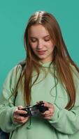 Vertical Young gamer girl holding controller, focused on finishing difficult videogame level. Woman gaming with gamepad and solving quests, isolated over studio backdrop, camera A video