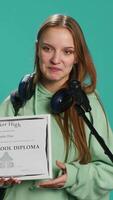 Vertical Happy student holding diploma talking in microphone, addressing audience, holding speech, studio background. Inspiring teenager using mic to share feeling during graduation ceremony, camera A video