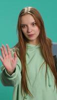 Vertical Assertive young woman doing stop hand gesture and talking. Annoyed girl doing firm halt sign gesturing, wishing to end concept, isolated over blue studio background, camera A video