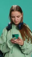 Vertical Happy girl receiving telephone call, saluting friends, using cellphone. Teenager having fun catching up with school colleagues during phone call, isolated over studio backdrop, camera A video