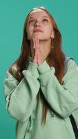 Vertical Hopeless young girl praying to deity for salvation. Religious teenager doing worship hand gesturing, asking for miracle, doing confession, isolated over studio background, camera A video