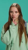 Vertical Stern woman doing shushing hand gesturing, irritated by noise, having negative mood. Girl placing finger on lips, doing quiet sign gesture, isolated over studio background, camera A video