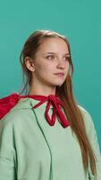 Vertical Portrait of jolly girl wearing superhero costume for Halloween, isolated over studio backdrop. Radiant teenage person dressed as comic book hero for event, showing courage and strength, camera A video