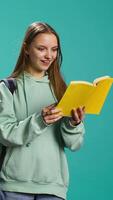 Vertical Teenage woman with book in hands showing appreciation for literature, isolated over studio background. Young reading enthusiast holding novel, enjoying reading hobby, camera B video