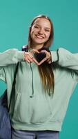 Vertical Portrait of friendly smiling woman doing heart symbol shape gesture with hands, being affectionate. Cheerful nurturing person showing love gesturing, isolated over studio background, camera B video