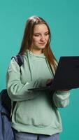 Vertical Radiant woman opening laptop to prepare for school exam, isolated over blue studio background. Upbeat student using notebook to prepare for university classes, studio backdrop, camera B video