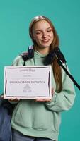 Vertical Overjoyed student celebrating achievement, holding diploma, using microphone to do speech, studio background. Woman using mic to share wisdom with colleagues after finishing school, camera B video