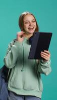 Vertical Radiant woman having funny conversation with friends during online teleconference using tablet, studio background. Upbeat girl having fun with mates during internet videocall on device, camera B video