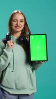 Vertical Portrait of woman presenting tablet with chroma key display, isolated over studio background. Young girl creating promotion with blank copy space mockup digital device, camera B video