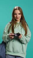 Vertical Young gamer girl holding controller, focused on finishing difficult videogame level. Woman gaming with gamepad and solving quests, isolated over studio backdrop, camera B video