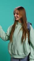 Vertical Radiant woman pointing finger towards empty space doing advertising, talking with audience. Smiling young girl doing presentation, showing copy text, studio backdrop, camera B video