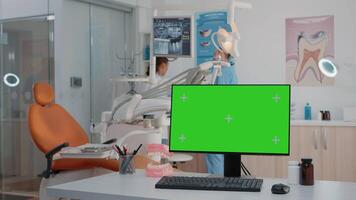 Horizontal green screen on computer in dental cabinet while dentist and assistant using oral care equipment for stomatological examination. Monitor with chroma key and isolated mockup template video