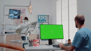 Man using monitor with horizontal green screen and talking to dentist about oral care in cabinet. Specialists working with dental tools for teethcare and isolated mockup template on computer video