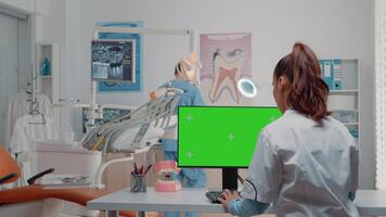 Dentist using computer with horizontal green screen on display. Specialist looking at monitor with chroma key and isolated template for oral care while asisstant using dental equipment video