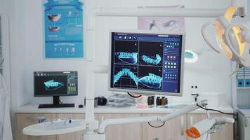 Closeup of monitor with tooth radiography images on it inside empty orthodontist stomatology hospital office room with nobody in it. Dental cabinet with medical tools prepared for healthcare treatment video