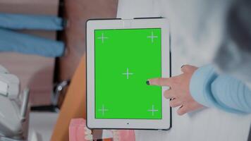 Vertical . Close up of dentist using green screen on tablet for teethcare in stomatology office. Orthodontist working with chroma key and isolated mockup template on device for oral care video