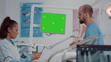 Dental team working with green screen on computer in cabinet for oral care. Dentist and assistant talking while looking at isolated background and mockup template for dentistry. video