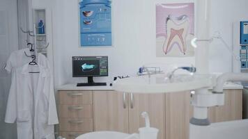 Empty stomatology orthodontist office room with medical drill and dental teeth xray images on monitor prepared for dental surgery. Hospital cabinet with nobody in it equipped with dentistry tools video