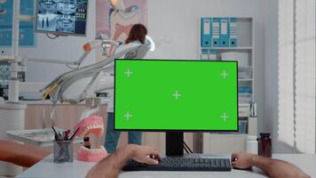 POV of assistant working with green screen on computer at dentist office. Man using monitor with chroma key and isolated mockup template for dentistry and teethcare in dental cabinet video