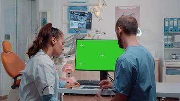 Nurse and dentist examining teeth layout using green screen on computer. Dentistry specialists looking at chroma key and isolated background on monitor for oral and dentition care video