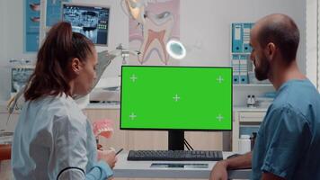 Oral care team looking at horizontal green screen on monitor while analyzing layout of teeth for dental examination. Assistant and dentist using tools and chroma key with mockup template video