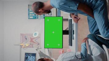 verticale . squadra di specialisti Lavorando con verde schermo su tenere sotto controllo nel dentale ufficio. dentista e uomo assistente utilizzando croma chiave con modello modello e isolato sfondo per orale cura video
