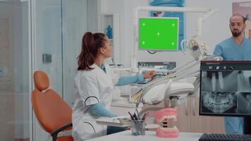 Woman using horizontal green screen on monitor in dental cabinet while man assistant giving teeth radiography for examination. Dentist working with mockup template and chroma key video