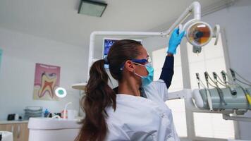 paciente pov dentro dental cadeira fazer realizando periódico dentes Verifica dentro moderno estomatológico clínica. odontologia médico iluminação a luminária e examinando pessoa vestindo proteção mascarar e óculos. video