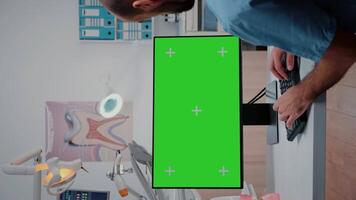 vertical . hombre enfermero trabajando con teclado y monitor con verde pantalla. odontología asistente mirando a croma llave con Bosquejo modelo en monitor para estomatológico cuidado. video