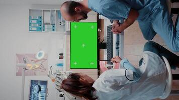 Vertical . Dentist and assistant looking at green screen on computer for teethcare examination. Man and woman working with dental tools and chroma key with mockup template for oral care. video