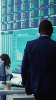 Vertical Chief financial officer examining capital funds and revenue data on annual reports in an office with a big screen, reviewing profit increase and budget allocation for a project. Camera B. video