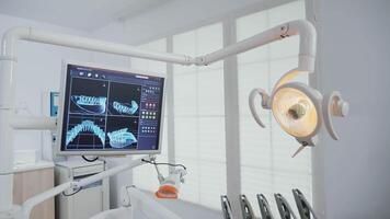 onthullend schot van leeg stomatologie orthodontisch kantoor met tanden x-ray diagnose afbeeldingen Aan monitoren uitgerust met tandheelkunde instrumenten klaar voor tandheelkundig chirurgie. tandarts kabinet voor mondeling zorg video