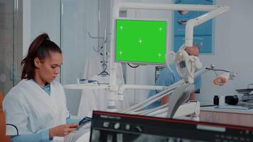 Woman analyzing green screen on monitor and teeth x ray for dental examination. Dentist using chroma key and mockup display for checkup while looking at radiography for oral care video