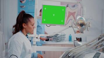 Dentist looking at monitor with horizontal green screen for oral care at dental office. Woman working as stomatologist with mockup template and isolated background for teethcare video