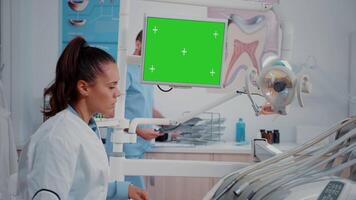 dentiste à la recherche à moniteur avec horizontal vert écran pour oral se soucier à dentaire bureau. femme travail comme stomatologue avec maquette modèle et isolé Contexte pour soins des dents video