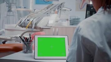 cerca arriba de digital tableta con horizontal verde pantalla en escritorio en odontología gabinete. dentista analizando aislado modelo y Bosquejo antecedentes con croma llave para estomatológico cuidado video