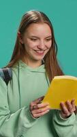 verticale adolescenziale donna con libro nel mani mostrando apprezzamento per letteratura, isolato al di sopra di studio sfondo. giovane lettura appassionato Tenere romanzo, godendo lettura passatempo, telecamera un' video