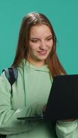 Vertical Radiant woman opening laptop to prepare for school exam, isolated over blue studio background. Upbeat student using notebook to prepare for university classes, studio backdrop, camera A video