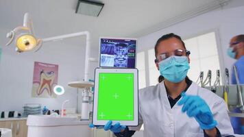 tandarts dokter tonen tablet met groen scherm, uitleggen tandheelkundig radiografie en diagnose voor tanden infectie. stomatologie specialist met gezicht masker richten Bij model, kopiëren ruimte, chroma Scherm video