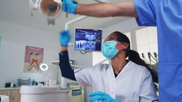 pov de patient dans une dentaire clinique séance sur chirurgie chaise vérification affecté masse. dentisterie équipe travail dans orthodontique bureau, éclairage le lampe et examiner personne, fermer visage dans médical masque. video