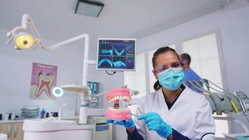 Patient pov of dentist showing correct way of cleaning teeth wearing in dental office using teeth medical skeleton accessory. Stomatolog wearing protection mask during heatlhcare check video