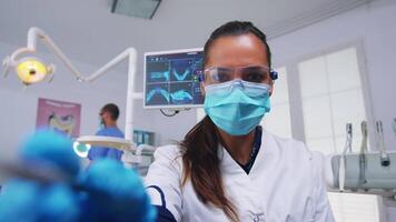 geduldig pov naar dokter in stomatologisch kantoor behandelen tanden van vrouw. orthodontisch specialist en Mens assistent werken vervelend maskers en handschoenen in modern tandheelkundig kliniek. video