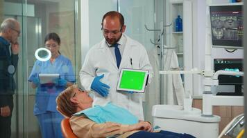 Dentist pointing at green screen display while patient lying on dental chair. Man explaining using monitor with green chroma key isolated chroma pc key mockup greenscreen display mock-up touchscreen video