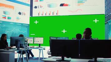 Diverse group of business specialists solve their daily tasks in control room with big greenscreen, analyzing big data numbers to ensure organizational progress. Startup management team. Camera B. video