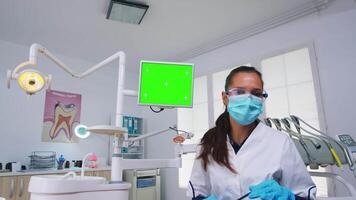 Patient pov of dentist explaining dental problem and diagnosis for teeth infection using monitor unit with green screen. Stomatology specialist pointing at mockup, copy space, chroma display video