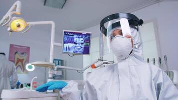 paciente pov de dentista en codicioso proteccion traje medición temperatura en moderno dental oficina con nuevo normal. estomatólogo vistiendo la seguridad engranaje en contra coronavirus durante cuidado del calor cheque de persona. video