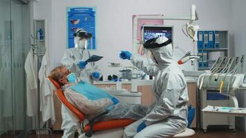 Dentist worker in personal protective kit examining dental x-ray before surgery. Concept of new normal dentist visit in coronavirus outbreak wearing protective suit and face shield video