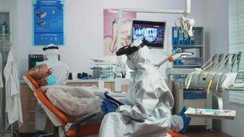 Dentist nurse in potective suit controlling patient temperature before dental examination during coronavirus pandemic. Concept of new normal dentist visit in coronavirus outbreak wearing protective suit and face shield video